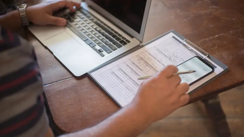 Personne remplissant un formulaire à côté d'un ordinateur portable