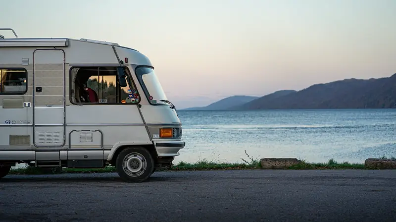 Avant d'un camping-car ancien garé sur une route goudronnée au bord d'un lac, au crépuscule