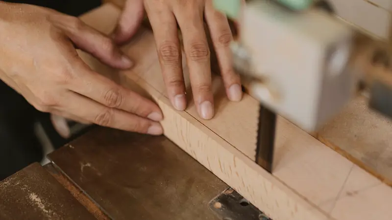 Mains guidant une pièce de bois clair dans une scie à ruban d'atelier