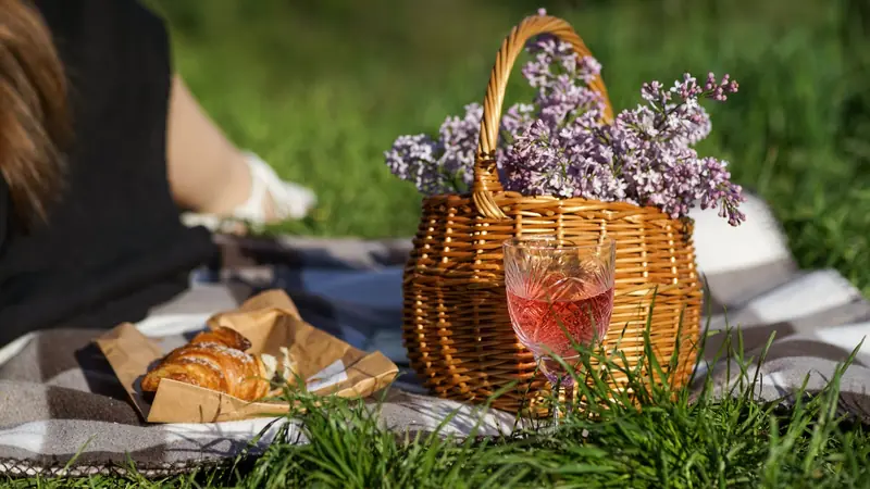 Verre de vin rosé foncé posé près d'un panier de pique-nique sur l'herbe