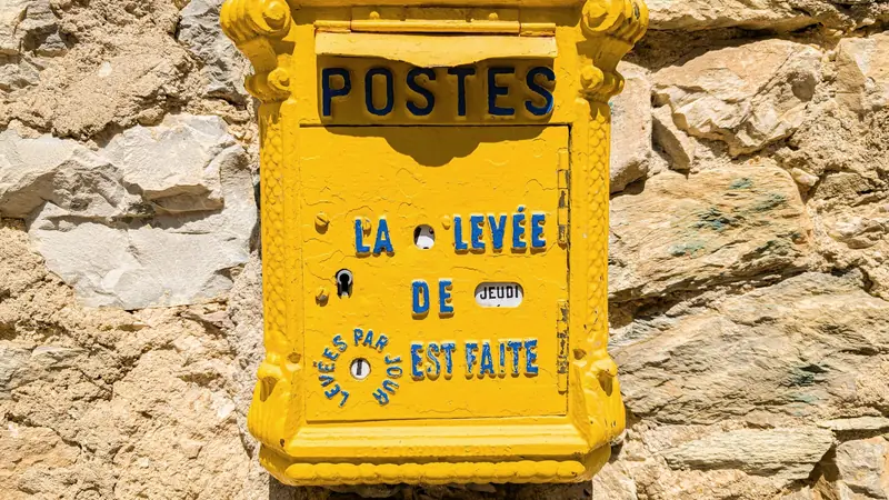 Boîte aux lettres jaune ancienne marquée Postes, fixée sur un mur en pierre
