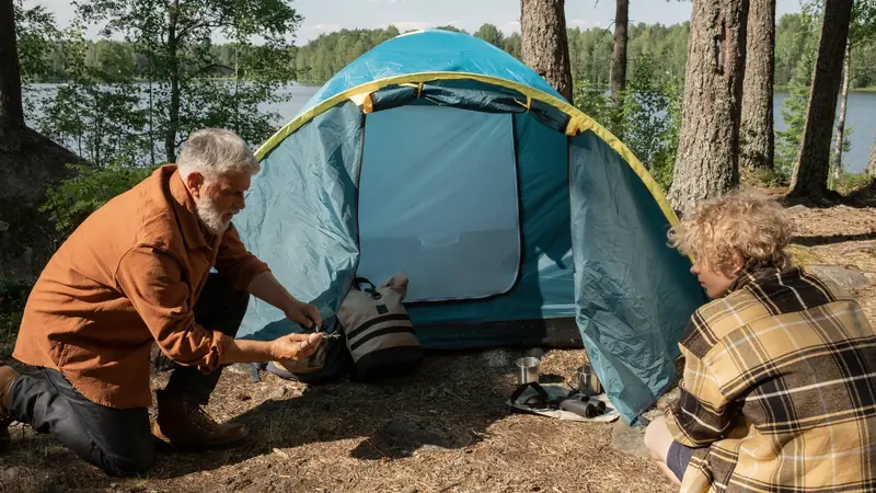 Un homme et un adolescent montent une tente sous les pins, au bord d'un lac