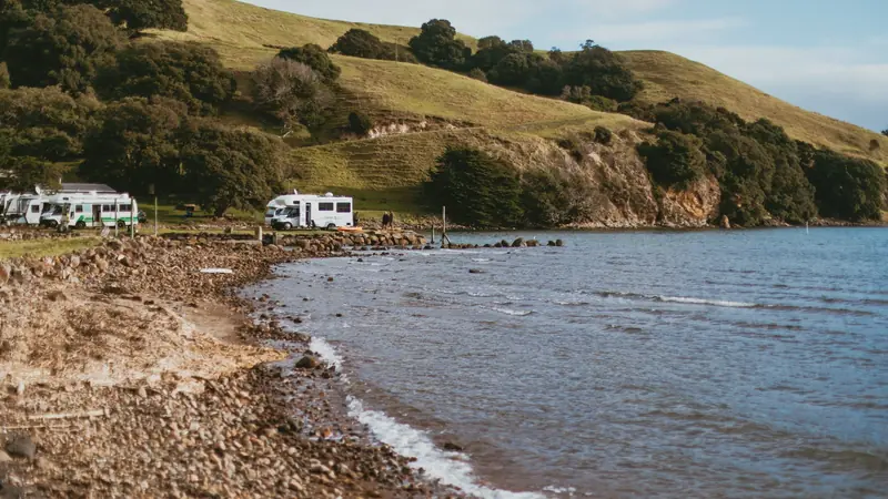 Camping-cars stationnés au bord d'une baie, au pied de collines boisées