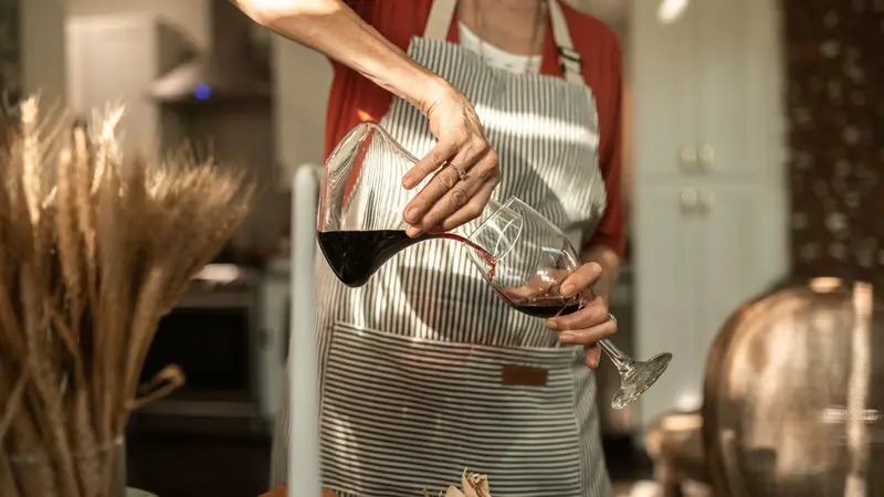 Personne versant du vin rouge d'une carafe dans un verre