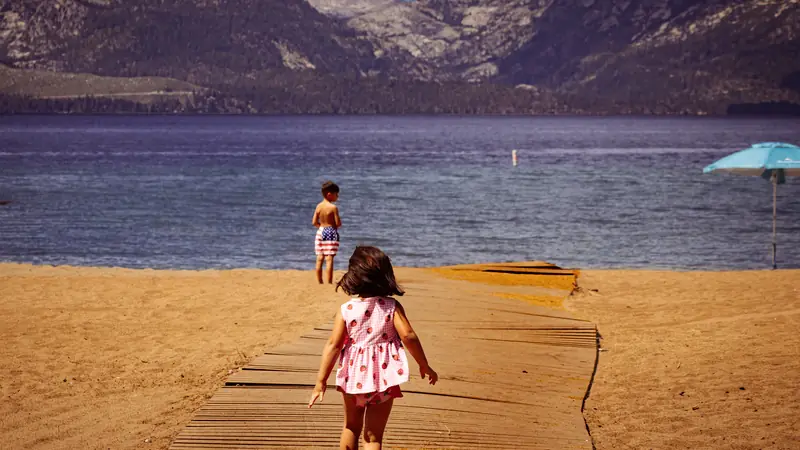 Enfants marchant sur un caillebotis vers une plage au bord de l'eau