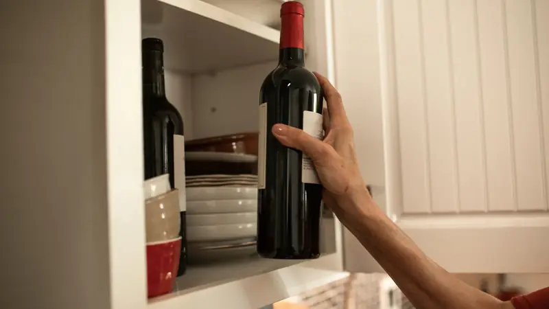 Main attrapant une bouteille de vin rouge rangée dans un placard