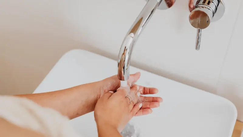 Personne se lavant les mains et les avant-bras à l'eau sous un robinet