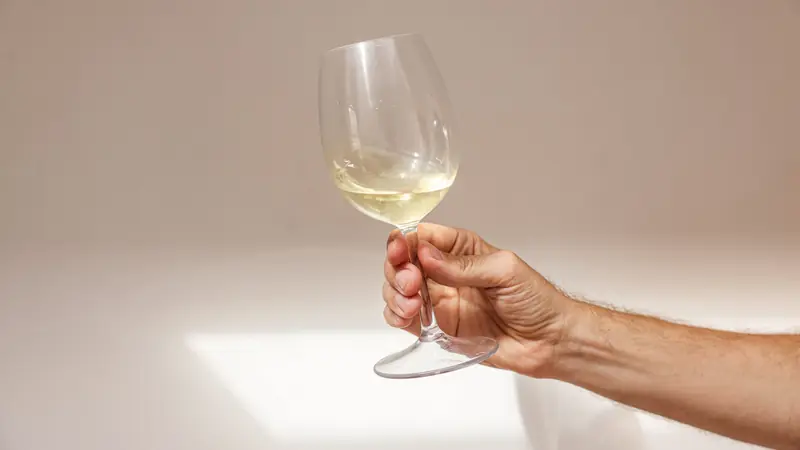 Main tenant un verre de vin blanc par le pied pour observer sa couleur