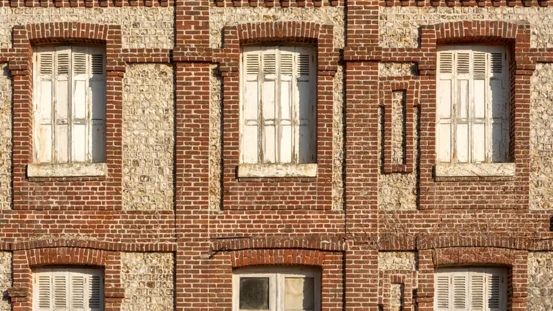 Façade ancienne en brique et silex aux volets fermés