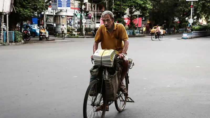Homme à vélo transportant une pile de journaux dans une rue presque vide