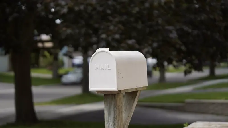 Boîte aux lettres blanche sur un poteau en bois au bord d'une rue résidentielle