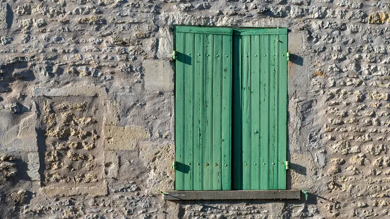 Volets verts fermés sur un mur en pierre