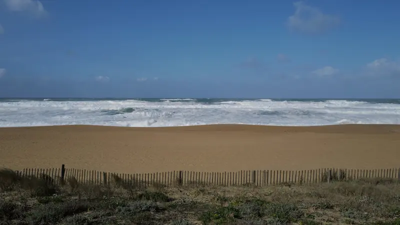 Grande plage de sable bordée de dunes sur la côte atlantique, avec des vagues