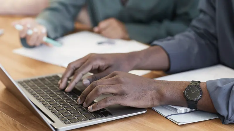 Gros plan sur des mains tapant sur le clavier d'un ordinateur portable posé sur une table en bois