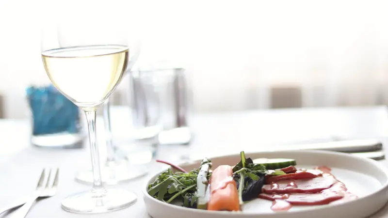 Verre de vin blanc posé sur une nappe blanche à côté d'une assiette
