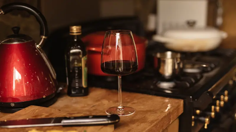 Verre de vin rouge sur un plan de travail, près d'une cocotte sur le feu