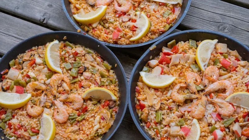 Trois poêles de paella aux crevettes et au citron sur une table en bois