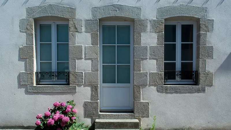 Façade de maison en pierre aux encadrements de granit, avec une porte et des hortensias