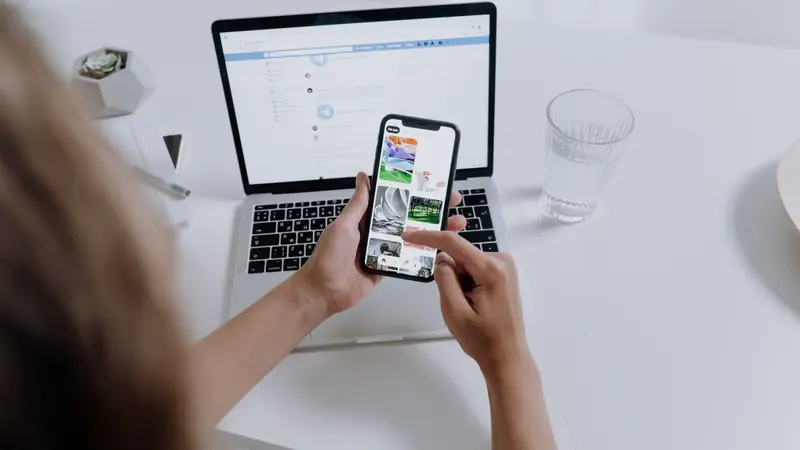 Personne tenant un smartphone devant un ordinateur portable ouvert sur un bureau blanc