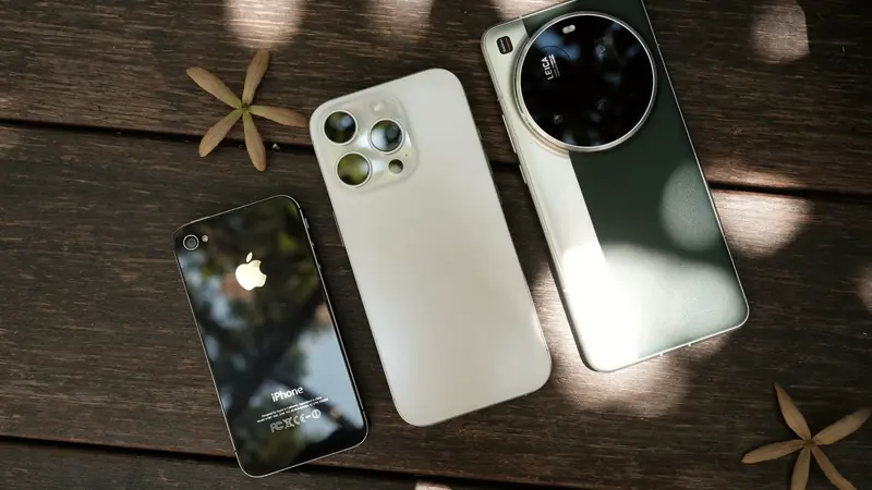 Un ancien iPhone et deux smartphones récents posés dos visible sur une table en bois