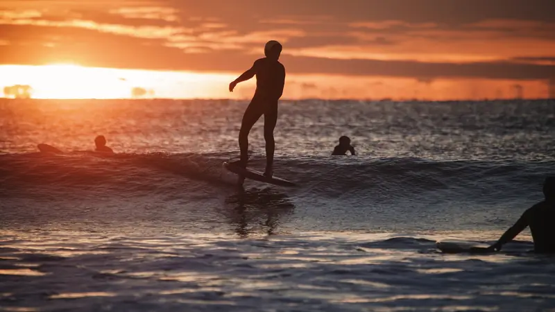 Silhouette d'un surfeur sur une vague au coucher du soleil