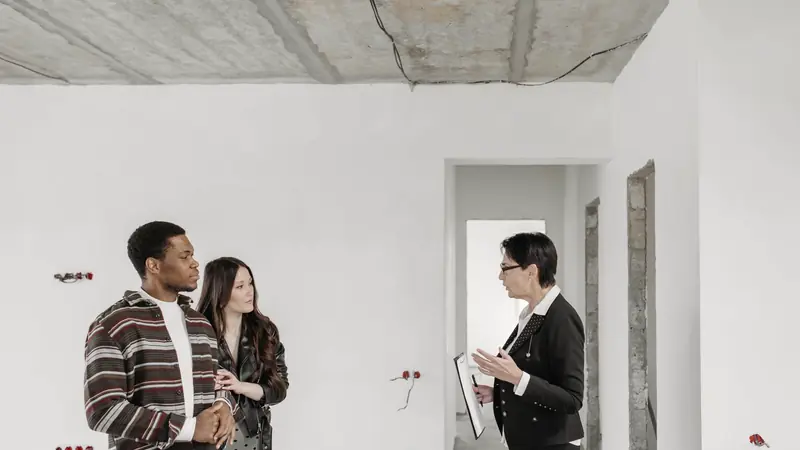 Femme tenant un porte-documents qui échange avec un couple dans un appartement en travaux aux murs bruts