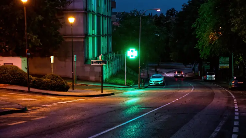 Croix verte lumineuse d'une pharmacie au bord d'une rue le soir